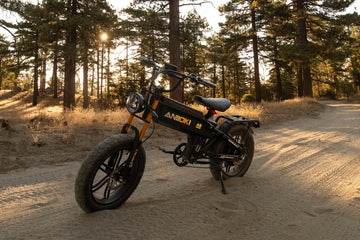 Aniioki A8 60V black long-range electric bike parked on a dirt forest trail during golden hour sunset, featuring its high-capacity battery system for riders wondering how long to charge a bike battery