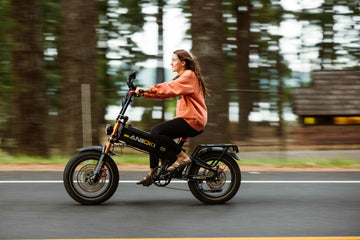 Is a 52V E-bike Battery Really Faster Than 48V? A Caucasian woman riding the powerful black and orange Aniioki 52V dual motor e-bike on a scenic tree-lined road, showcasing its strong torque and excellent climbing capability.