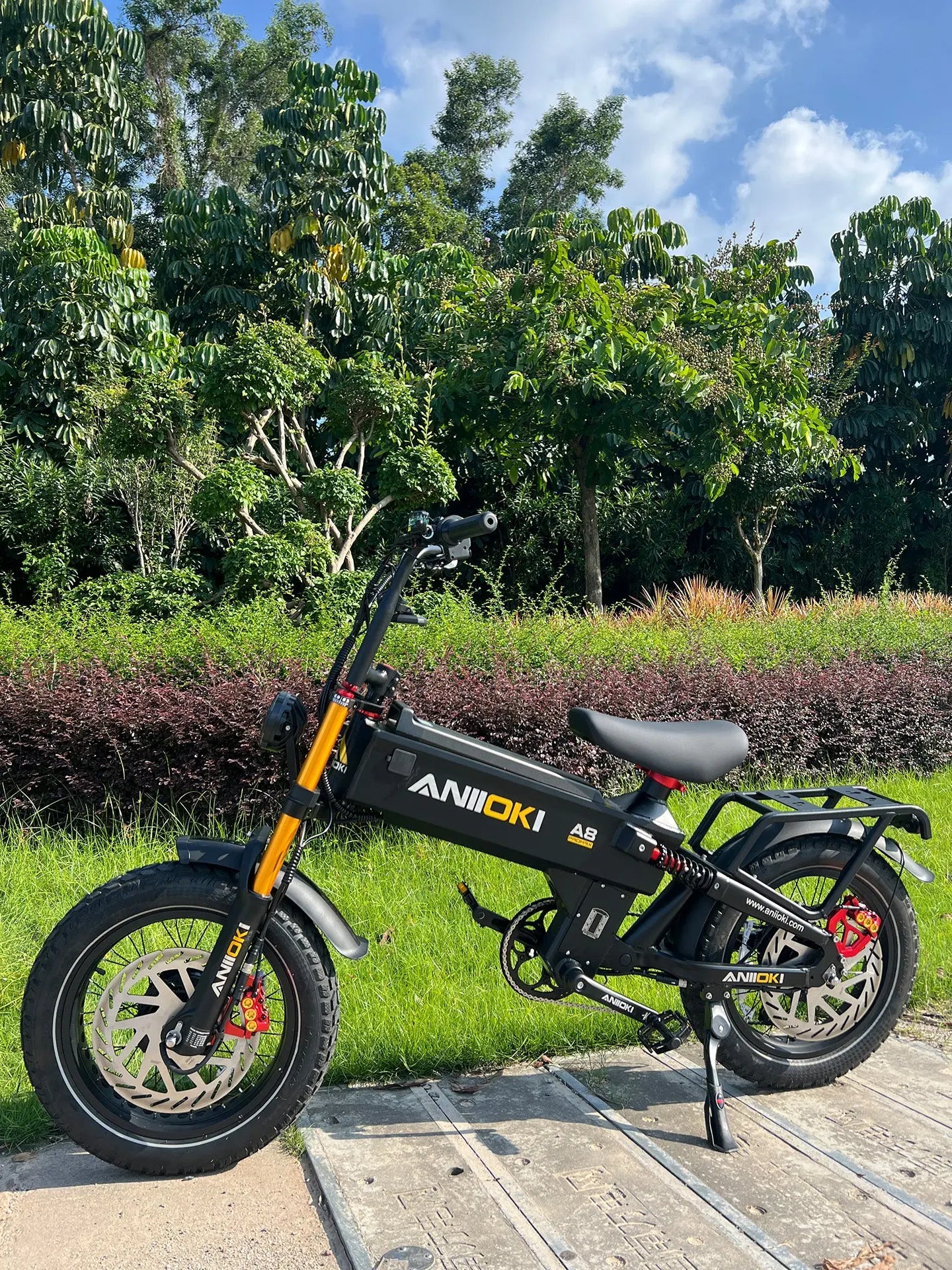 a black Aniioki A8 Pro Max 52V dual motor ebike parked on a garden path with lush green trees, showcasing this long range ebike and fast electric bike.