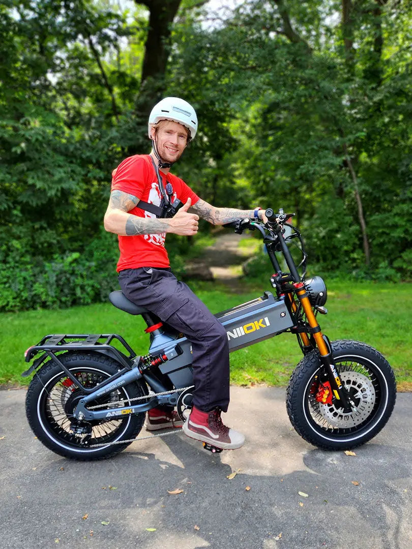 A white man giving a thumbs up while sitting on a matte gray Aniioki A8 Pro Max for sale, highlighting the comfort and power of the fastest dual motor ebike.
