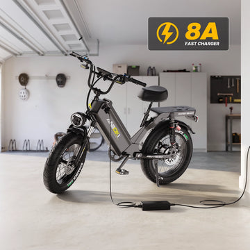 Matte gray Aniioki AQ177 60V long range ebike connected to an 8A fast charger on a stand inside a home garage for rapid battery charging.